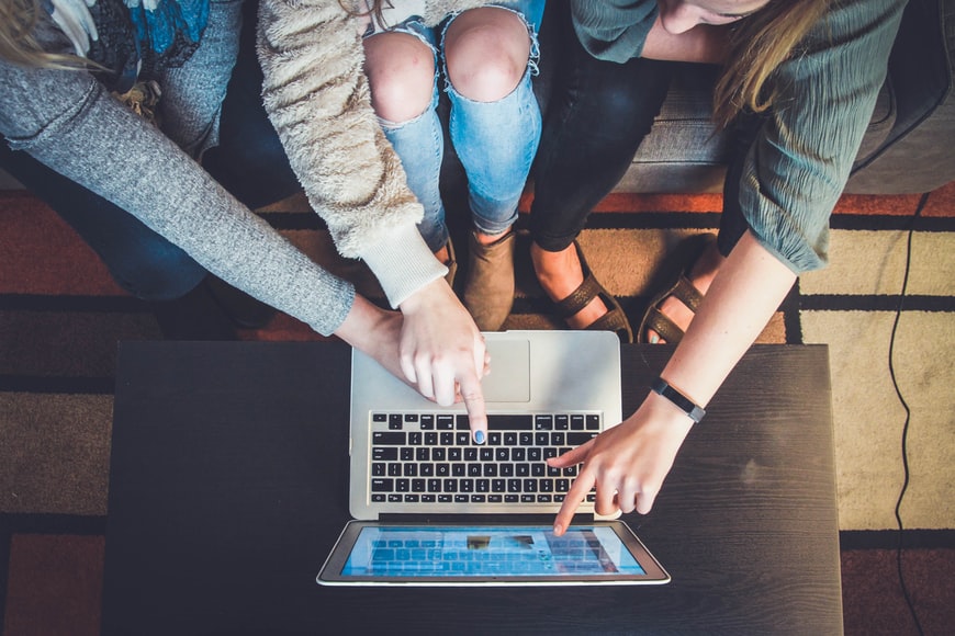 An aerial shot of three students sitting close together and pointing to a laptop screen